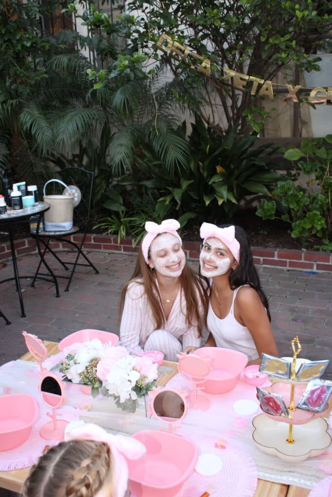 Two guests at a spa party setup with pink basins and supplies.