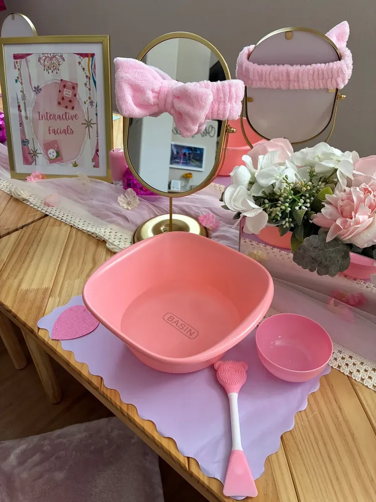 A pink spa table with headbands, basin, brush, towels, and supplies.